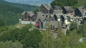 Un village de montagne aux maisons traditionnelles en bois, avec un ciel dégagé et des montagnes enneigées en toile de fond.