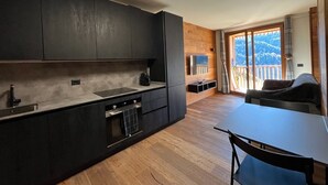Une cuisine moderne avec des meubles de couleur sombre, un four encastré et un coin repas comprenant une table et des chaises.