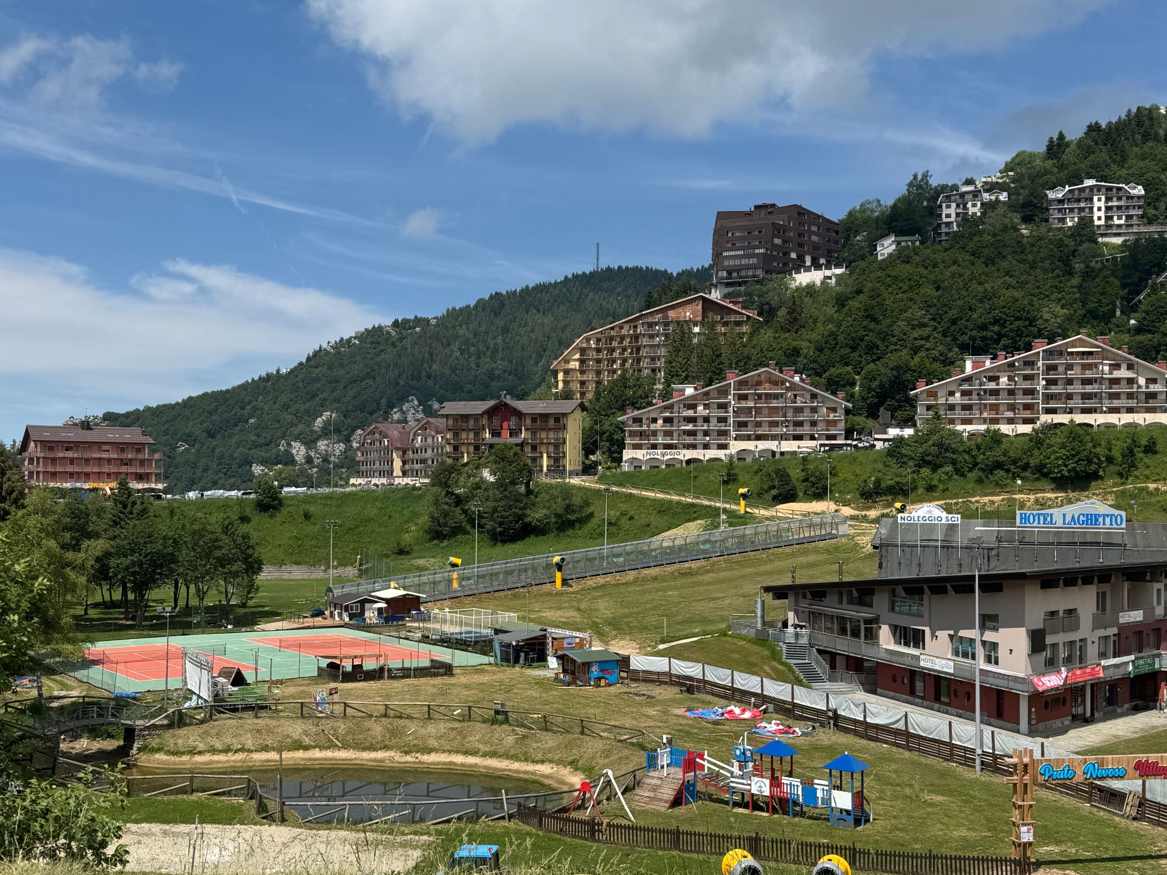 Ein Hotel mit mehreren Etagen, einem Tennisplatz und einem Spielplatz.