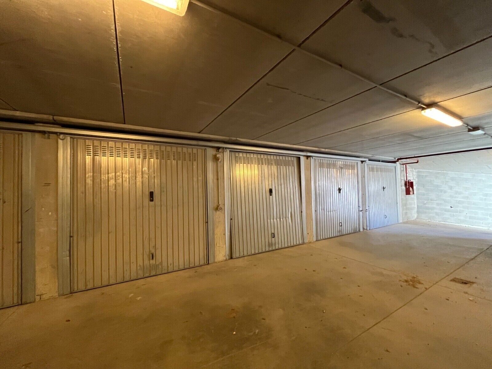 Un long couloir désert, avec des portes en métal et un sol en béton.