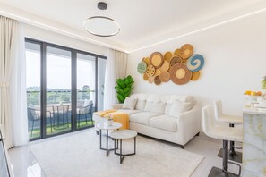 A modern living room with a white sofa, a coffee table, and a dining area with a white chair. - Cozy 1-bedroom Apartment With Modern Amenities in Nairobi (Nairobi)