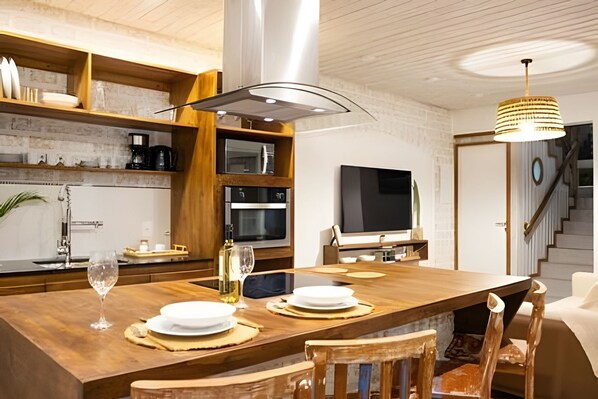 A modern kitchen with wooden cabinetry, a built-in oven, and a dining area with a large table and chairs. - Casa Vivonge (Tibau do Sul)