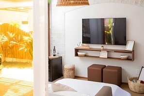 A modern hotel room with a bed, a TV mounted on the wall, a small shelf with decorative items, and a view of the outside. - Casa Vivonge (Tibau do Sul)