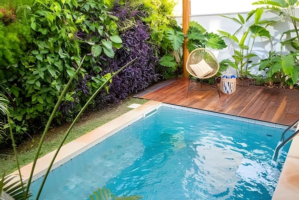 A rectangular pool with a wooden deck and a variety of plants around it.