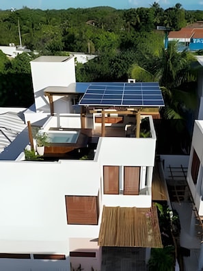 A residential building with a solar panel roof, a wooden pergola, and a view of surrounding greenery.