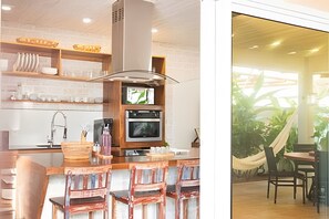 A kitchen with a TV, oven, and bar area with chairs. - Casa Vivonge (Tibau do Sul)