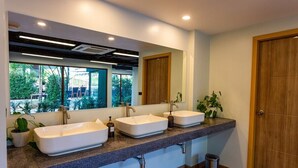 Une salle de bain avec trois lavabos, un grand miroir et une vue sur la verdure à l’extérieur.