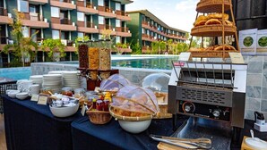 Un buffet proposant une variété de plats, un barbecue et une vue sur un bâtiment d’hôtel doté de balcons.