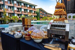 Ein reichhaltiges Buffet mit verschiedenen Speisen, einem Grill und Blick auf ein Hotelgebäude mit Balkonen.
