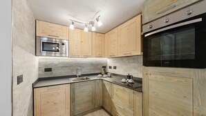 A modern kitchen with wooden cabinets, a built-in microwave, a double oven, and a countertop with a kettle and coffee maker. - Holiday Home 'Lueur De La Rouja' with Mountain View (Champoluc)