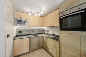 A modern kitchen with wooden cabinets, a built-in microwave, a double oven, and a countertop with a kettle and coffee maker.