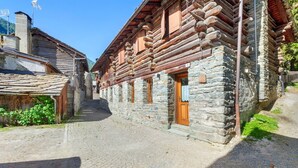 A narrow cobblestone street flanked by traditional log buildings with stone walls and wooden doors. - Holiday Home 'Lueur De La Rouja' with Mountain View (Champoluc)