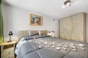 Ein Schlafzimmer mit einem Bett, einem Nachttisch, einer Lampe, einem Kleiderschrank und einem Bild an der Wand.