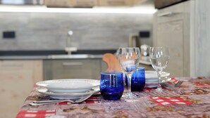 A dining table with plates, glasses, and cutlery, set in a kitchen with wooden cabinets and a tiled backsplash. - Holiday Home 'Lueur De La Rouja' with Mountain View (Champoluc)