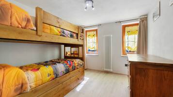 Una camera con un letto a castello, un comò in legno, una finestra con tende e un termosifone.