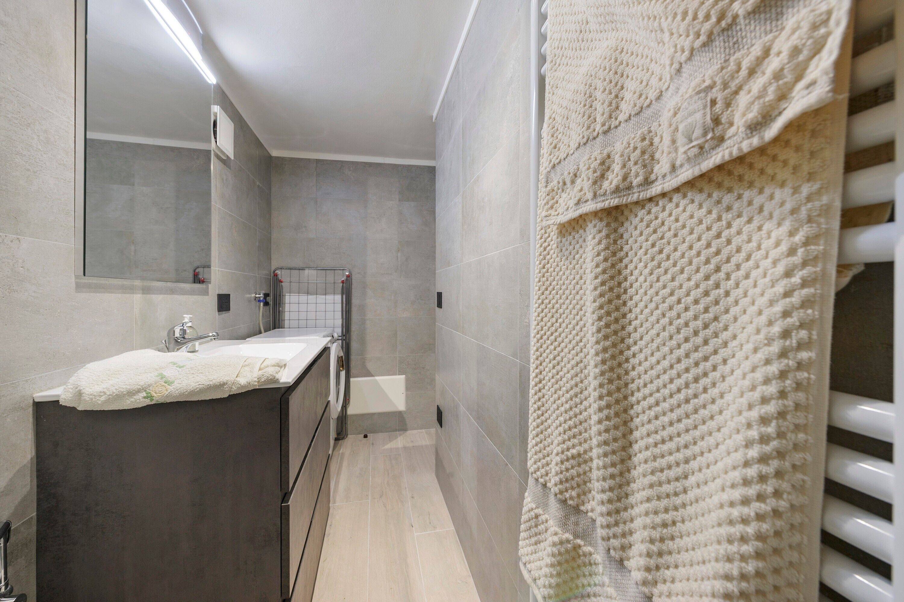 Ein modernes Badezimmer mit Waschbecken, Spiegel, Handtuchhalter und Duschbereich.