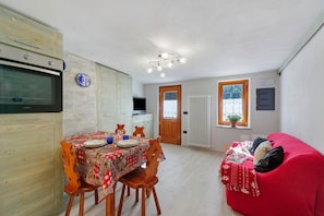 Eine kompakte Küche mit Einbauofen, einem Esstisch mit Stühlen, einem roten Sofa und einem Fenster mit Blick ins Grüne.