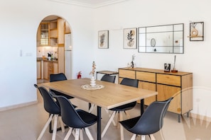 Ein moderner Essbereich mit Holztisch und schwarzen Stühlen, eine Küche mit Holzausstattung und ein großer Spiegel an der Wand.