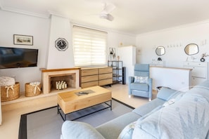 Ein modernes Wohnzimmer mit einer Couch, einem Couchtisch, einem Kamin, einem Fernseher und einem Deckenventilator.