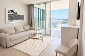 A modern living room with a sofa, a coffee table, and a chair. There is a large window with a view of the city.