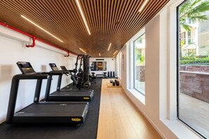 A gym with treadmills, exercise equipment, and a view of a brick wall and greenery outside. - Ocean's Edge Suite at 42 Eilat (Eilat)