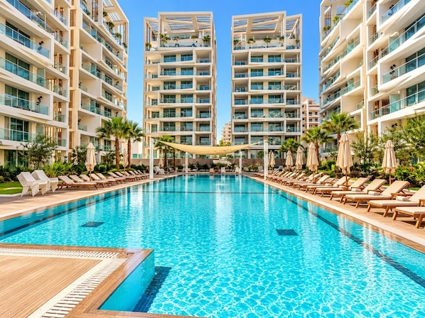 A modern hotel with a central swimming pool surrounded by lounge chairs and palm trees.