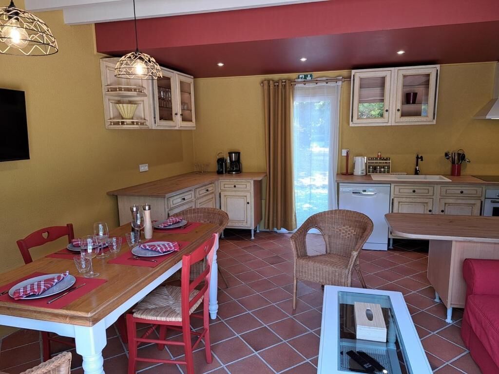 Un coin repas avec une table en bois, des chaises rouges et une table basse en verre. On y trouve des armoires avec des portes en verre et une fenêtre avec des rideaux.
