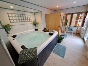 A spa room with a hot tub, wooden cabinets, a chair, and potted plants.