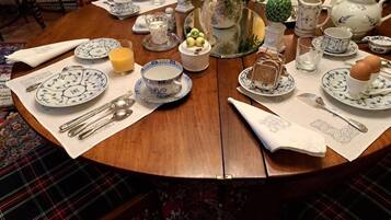 Een ronde houten tafel gedekt voor het ontbijt, met theeservies, een bloemenvaas en een decoratieve fruitschaal.