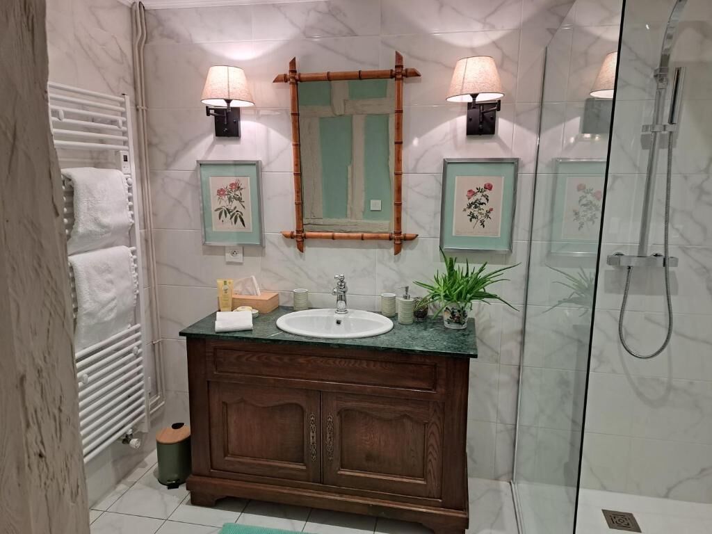 Bagno con parete in marmo, mobile lavabo in legno, lavandino, due lampade a parete, un quadro con fiori e box doccia in vetro.