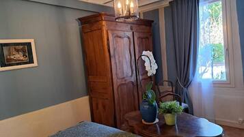 A room with a wooden cabinet, a table with a vase and plant, a framed picture on the wall, and a window with curtains.