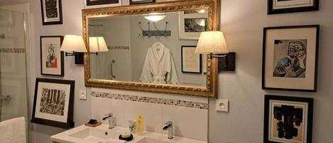 Une salle de bain dotée d’un grand miroir, de deux lavabos, d’une commode et d’œuvres d’art encadrées accrochées aux murs.