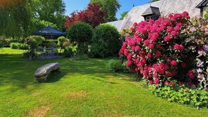 A garden with a gazebo, a stone bench, and a building with a sloped roof.