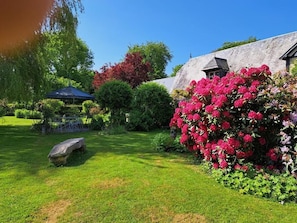 A garden with a gazebo, a stone bench, and a building with a sloped roof.