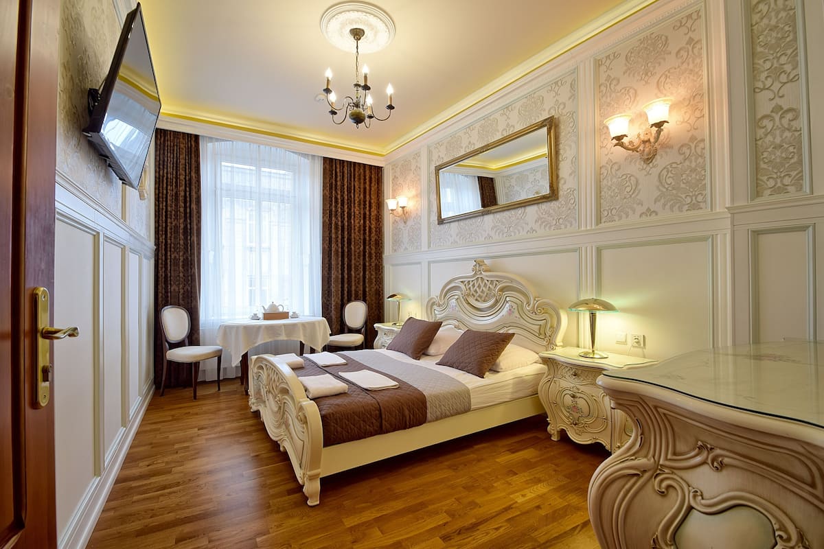 Ein stilvoll eingerichtetes Schlafzimmer mit einem großen Bett, einem Nachttisch, einem Spiegel und einem an der Wand befestigten Fernseher.