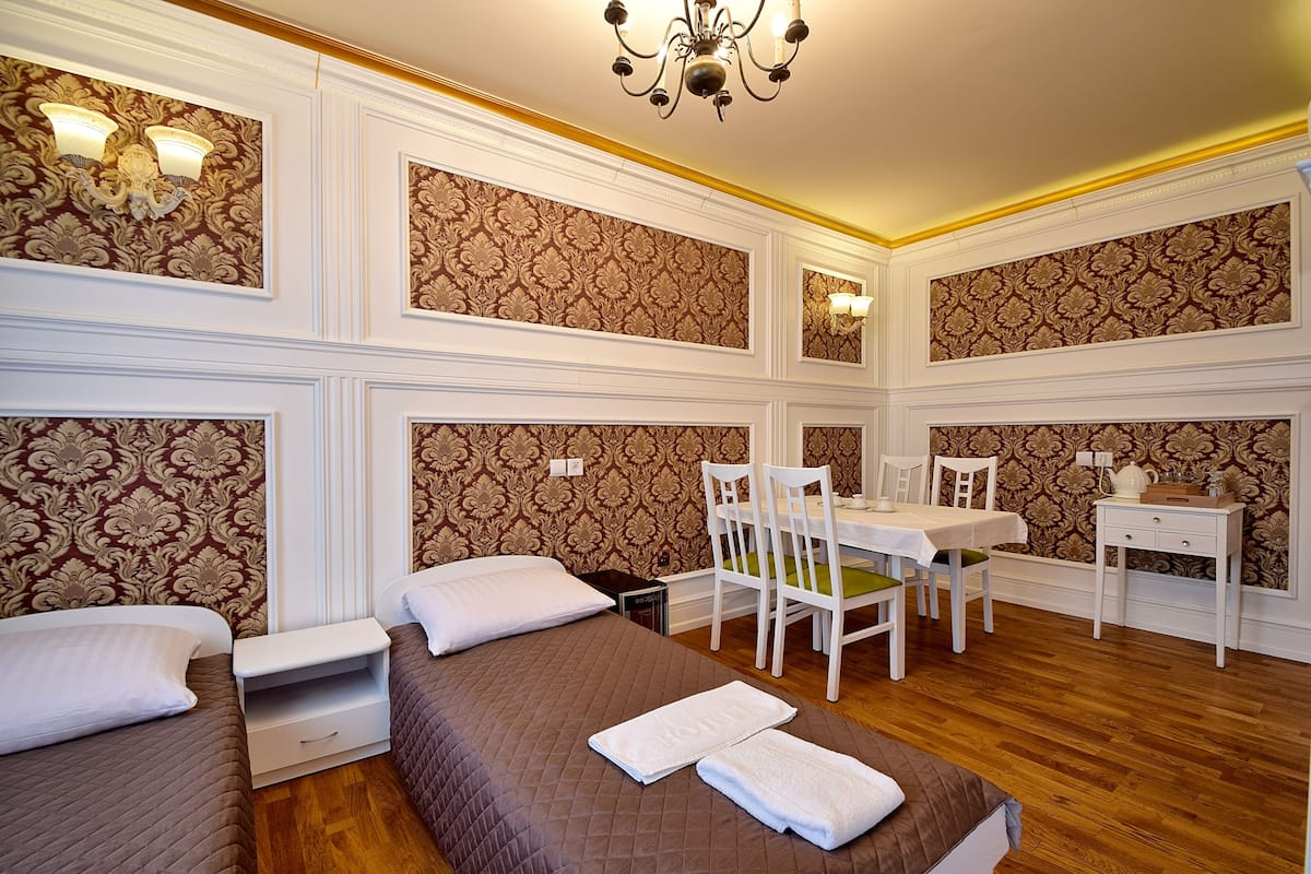 Ein Hotelzimmer mit zwei Betten, einem Esstisch, Stühlen, einem kleinen Tisch mit Lampe und Wandtapete mit Muster.