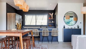 Een moderne keuken met een eetgedeelte, met een houten tafel, rieten stoelen en een groot raam.