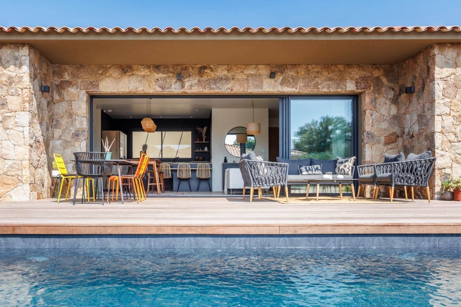 Zona junto a la piscina con muros de piedra, mobiliario exterior y vista hacia la casa.