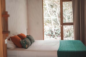 Un lit avec des oreillers, une couverture verte et une vue sur les arbres par la fenêtre.