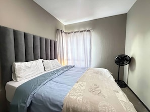 Ein Schlafzimmer mit Bett, Vorhängen, einem Standventilator und einer Deckenleuchte.