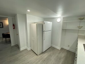 Une cuisine avec un réfrigérateur blanc, un plancher en bois et des murs blancs.