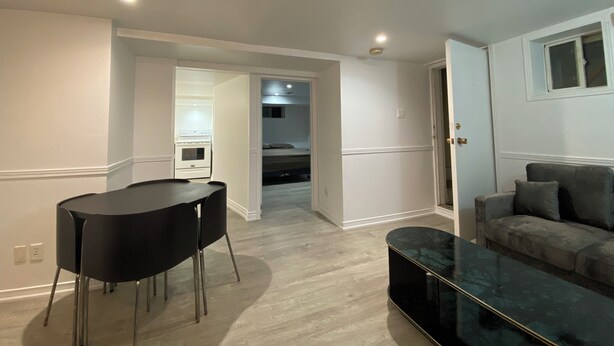 A modern living room with a dining area, a sofa, and a kitchen in the background. - Amazing apartment in house Basement (Toronto)