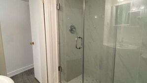 A modern bathroom with a glass shower enclosure, a white sink, and a door leading to another room. - Amazing apartment in house Basement (Toronto)
