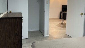 A bedroom with a wooden dresser, a bed, a closet, and a television in the adjacent room. - Amazing apartment in house Basement (Toronto)