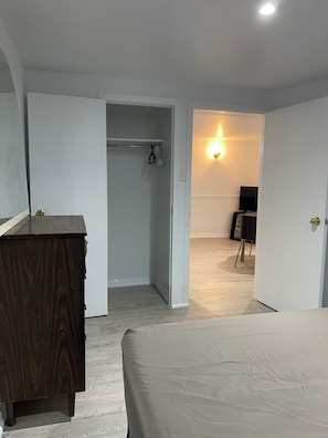 Une chambre à coucher avec une commode en bois, un lit, une armoire et un téléviseur dans la pièce adjacente.