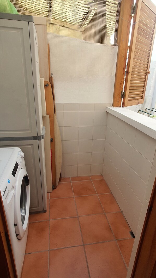 A small laundry room with a washing machine, a drying rack, and a tiled floor.