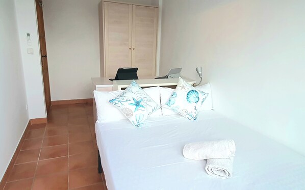 A bedroom with a bed, a desk with a chair, a laptop, and a lamp.