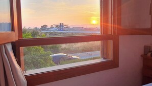 Une fenêtre donnant sur un coucher de soleil, une grue et une voiture sur la route.