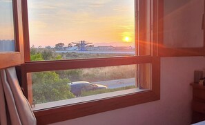 A window with a view of a sunset, a crane, and a car on the road.