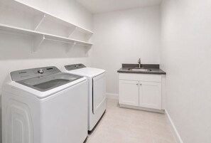 Een wasserette met een wasmachine, droger en een wasbak met kastjes.